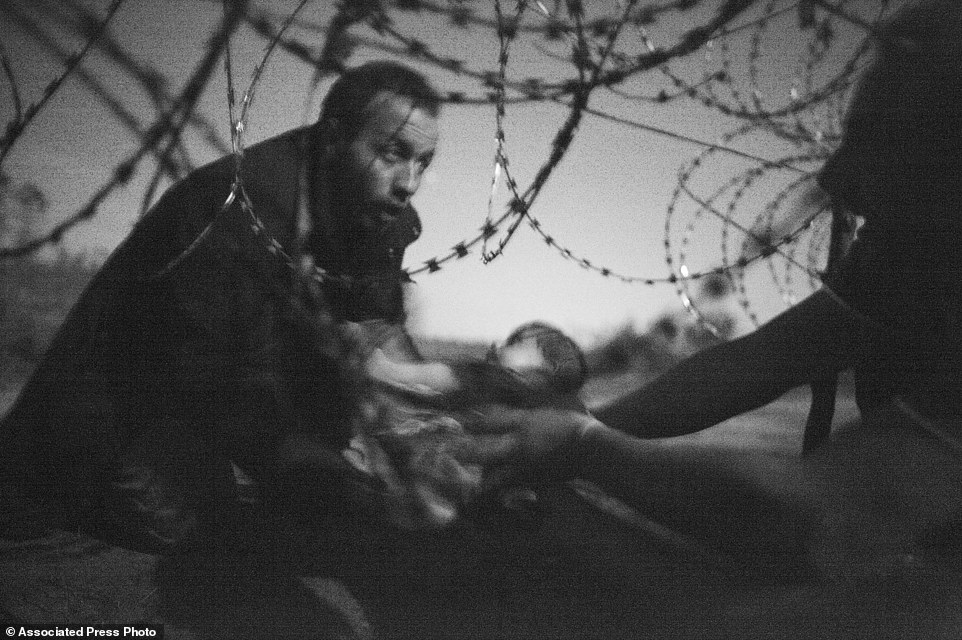 In this image released by World Press Photo shows the World Press Photo of the Year titled "Hope for a new Life" by photographer Warren Richardson. The picture also won a first prize in the Spot News singles category and shows a man passing a baby through the fence at the Serbia-Hungary border in Roszke, Hungary, Aug. 28, 2015. (Warren Richardson, World Press Photo via AP)