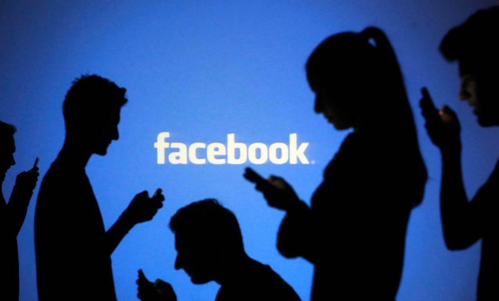 People pose with laptops in front of projection of Facebook logo in this picture illustration taken in Zenica