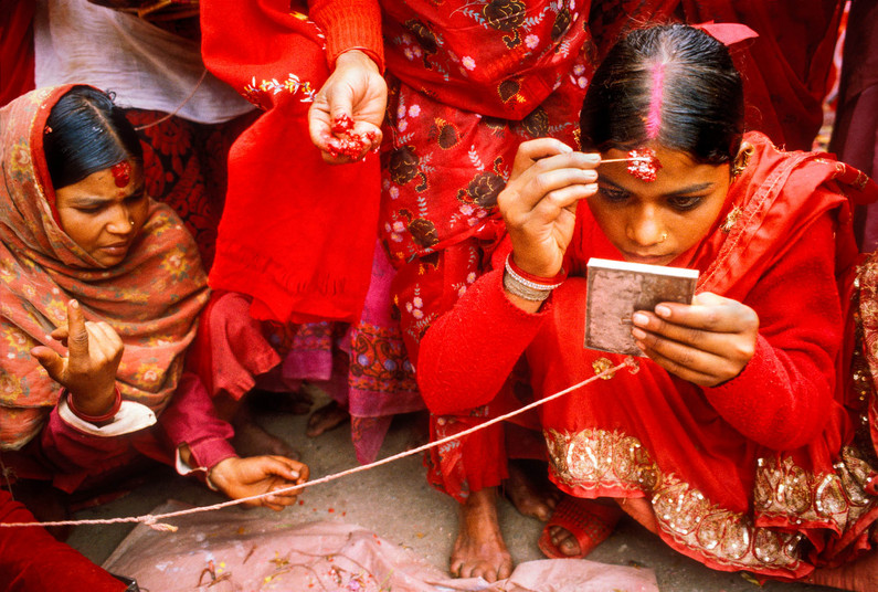 Nepali women in red saris apply colorful makeup at Teej festival